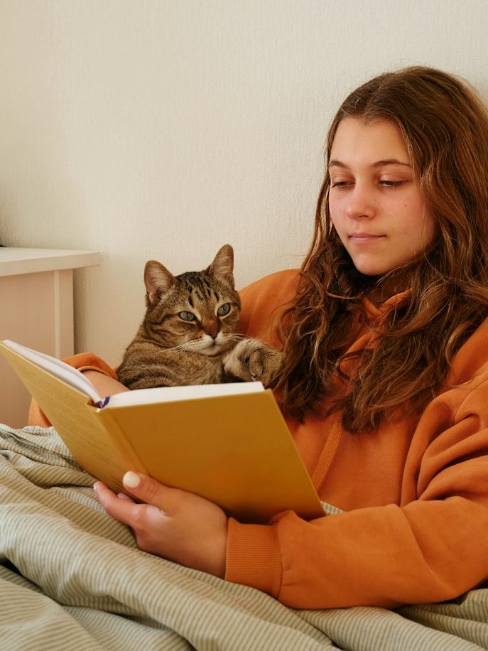 Eine lesende Person mit langen Haaren und einem Kätzchen auf dem Schoß.