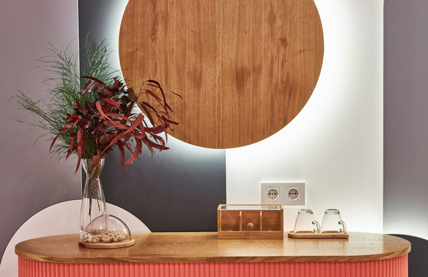 die Wohnung katzengerecht gestalten Holztisch mit runder Wanddekoration, Vase mit Blumen und modernen Elektroanschlüssen.